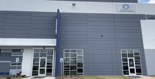 Direct front view of Greentech Renewables building. The building is grey with blue and white accents. There are large "CED" letters on the ledge and a full color logo with "Greentech Renewables" on the front and doors.